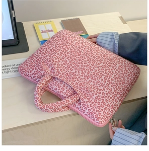 Detailed view of pink leopard print laptop sleeve with handles on a wooden desk