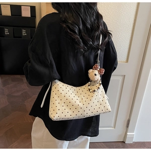 Detail of cream crossbody bag with brown polka dots and plush bear charm on a model