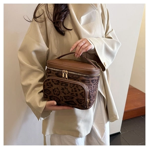 Detail view of leopard print suede makeup bag with golden zippers and leather handle