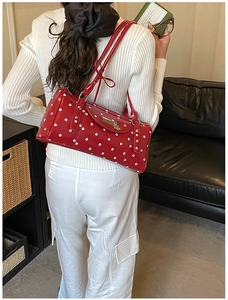 Retro red cylindrical shoulder bag with white polka dots on a stylish woman's shoulder