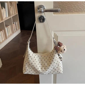 Polka dot hobo bag with cute plush bear charm hanging on a white door handle