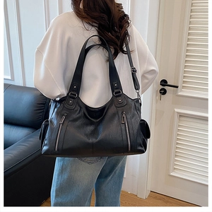 Detail view of black lychee leather tote bag with vertical zippers on a model back side