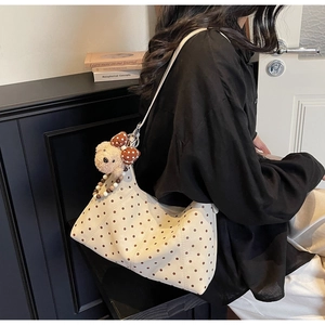 Detail of a creamy white polka dot crossbody bag featuring a cute plush bear charm accessory
