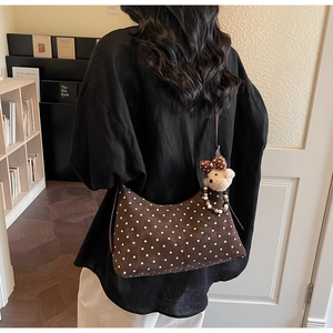 Detail of dark brown polka dot shoulder bag with a cute plush bear charm in a cozy room