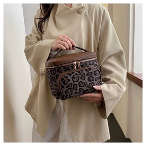 Close-up of leopard print cosmetic bag with brown leather handle and gold zippers