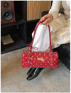 Detail of red polka dot cylinder handbag featuring a decorative bow and metal heart charm