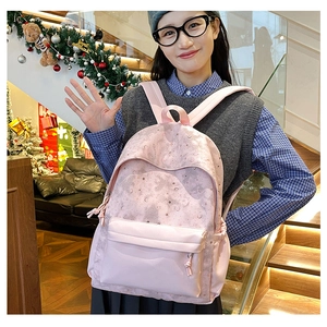 Detail of light pink backpack showing silver moon and star patterns with front zipper pocket