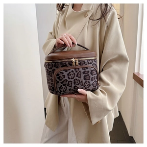 Detail of leopard print makeup bag with brown leather handle and gold zippers