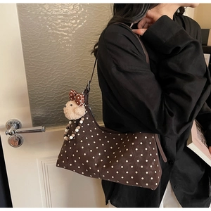 Brown polka dot shoulder bag with bear plush pendant shown on model in a soft indoor light