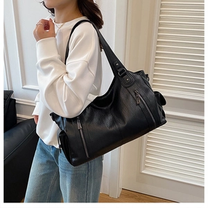 Model wearing a large black leather tote bag with functional zippers and dual handles