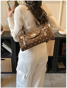 Sac sous le bras marron à pois en cuir verni porté par un mannequin en intérieur