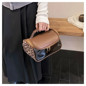 Detail of leopard print cosmetic bag with brown leather handle and transparent PVC panel