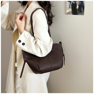 Detail of dark brown leather tote bag with side drawstrings worn with a white coat