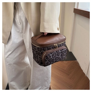 Detail of leopard print vanity case with brown leather handles held by a model