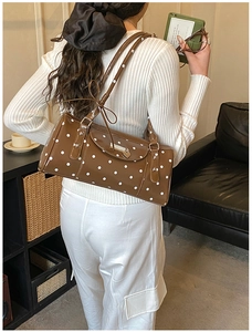 Detail of dark brown polka dot shoulder bag with heart-shaped metal pendant charm