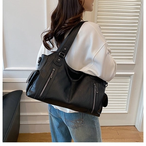 Detail of black pebbled leather tote bag with functional zippers and wide straps
