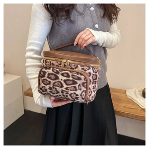 Detail of leopard print vanity case with brown leather handle held by a model