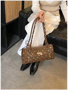 Detailed view of brown patent leather barrel bag with white polka dots and heart charm