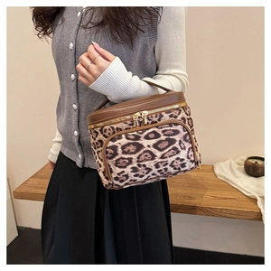Detail of leopard print cosmetic bag with brown leather trim and golden double zippers