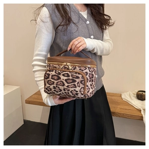 Detail of leopard print cosmetic bag with brown leather trim and golden metal zippers