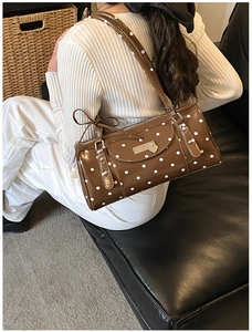 Close-up of vintage brown polka dot underarm bag with metallic heart charm on model