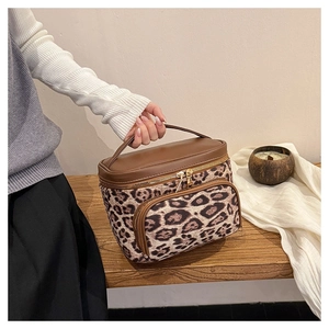 Detail of leopard print vanity bag with brown leather handle on a wooden bench