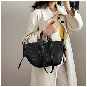 Detail of black tote bag featuring contrast stitching and drawstring knot on a long coat