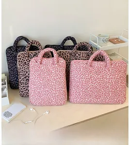 Three leopard print laptop sleeves with handles and zippers on a warm wooden desk