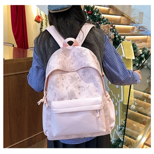 Pink backpack with moon and stars print worn by model in a cozy indoor setting
