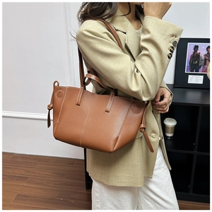 Detail of caramel leather tote bag with white contrast stitching and knotted side ties