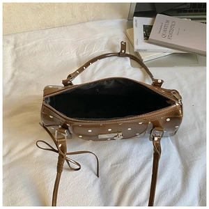 Detailed top view of a brown polka dot cylindrical shoulder bag with heart hardware
