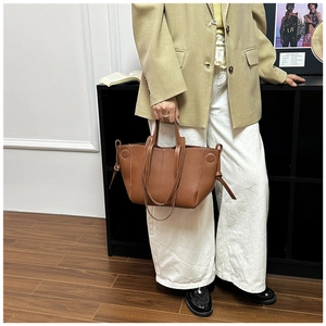 Close-up of brown leather tote bag with white stitching and decorative side knots