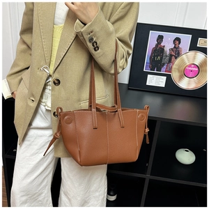 Detail of a brown leather tote bag with white contrast stitching and side drawstring knots