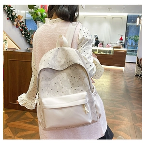 Rear view of a model wearing a beige backpack with star and moon prints in a cafe setting