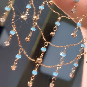 Makro-Detail der goldenen Quastenkette mit blauen Frostperlen und funkelnden Kristallen