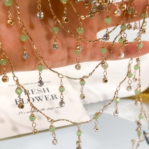 Detail einer mehrlagigen Goldkette mit grünen facettierten Perlen und Kristallen