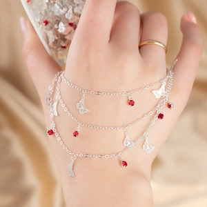 Detail of silver layered bracelet featuring red gemstone charms and butterfly pendants