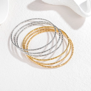 Detail van zes goud- en zilverkleurige stapelbare armbanden met geometrische gravures