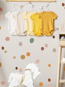 Detail of five yellow baby bodysuits hanging on a wooden rack in a nursery room