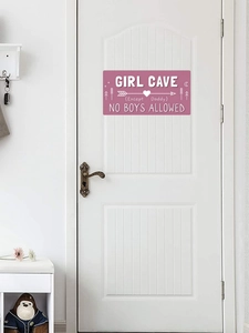 Panneau Girl Cave rose avec lettrage blanc suspendu sur une porte de chambre blanche