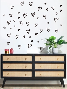 Detail of hand-drawn black heart wall decals on a white wall above a black cabinet