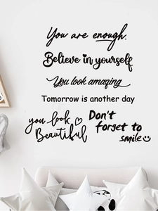 Détail de stickers muraux avec citations inspirantes noires sur mur blanc avec coussins