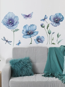 Adesivi murali con fiori blu e farfalle applicati sopra un divano grigio in salotto