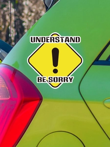Detail of yellow diamond road sign car sticker with exclamation mark and text on green vehicle