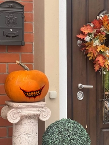 Nahaufnahme von Halloween-Kürbis mit gruseligem Lächeln auf Steinsockel vor Backsteinwand