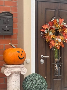 Outdoor porch decor with smiling Halloween pumpkin on stone base and autumn leaf wreath
