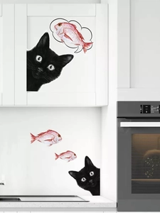 Detail of self-adhesive black cat peeping wall sticker with a red fish on a kitchen cabinet
