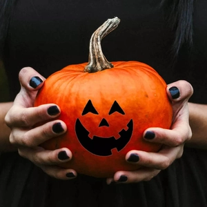 Vibrant orange Halloween pumpkin with black face held by hands against dark background