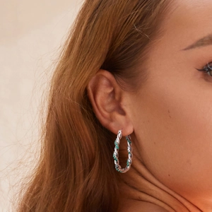 Élégantes créoles torsadées en argent avec zircons verts portées par un mannequin