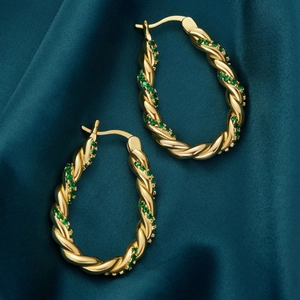 Gros plan détaillé des boucles d'oreilles ovales torsadées dorées aux pierres vertes